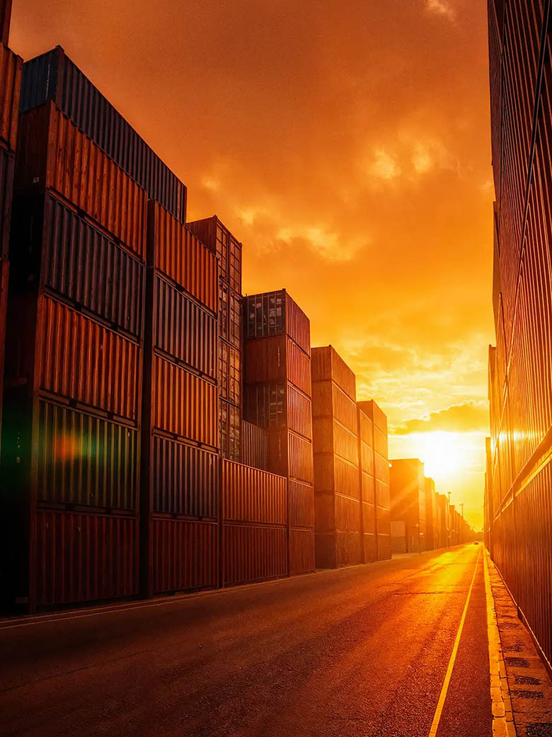 Stacked shipping containers lining a container-yard road at sunset